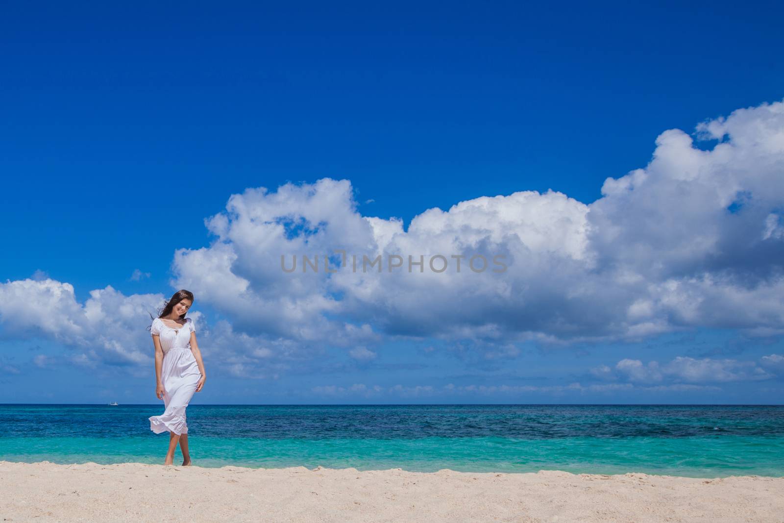 Woman in white dress walking on tropical beach, tropical sea on background