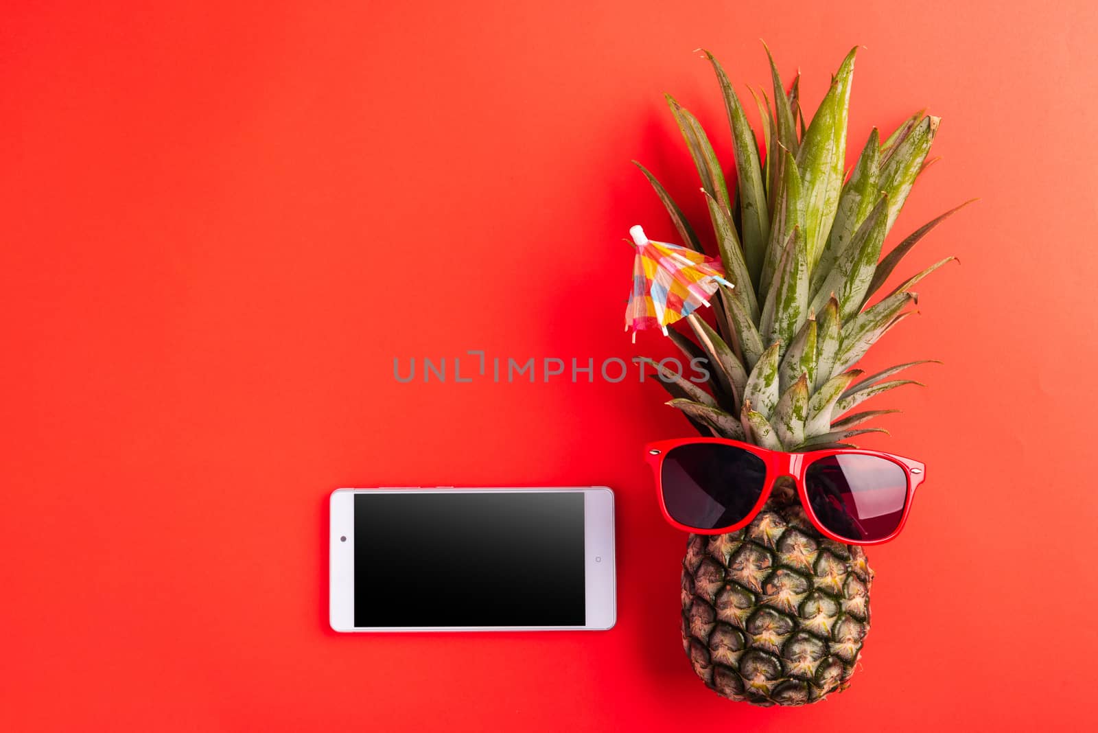 Celebrate Summer Pineapple Day Concept, Top view of funny pineapple wear red sunglasses and smartphone blank screen, isolated on red background, Holiday summertime in tropical, minimal stylish fruit