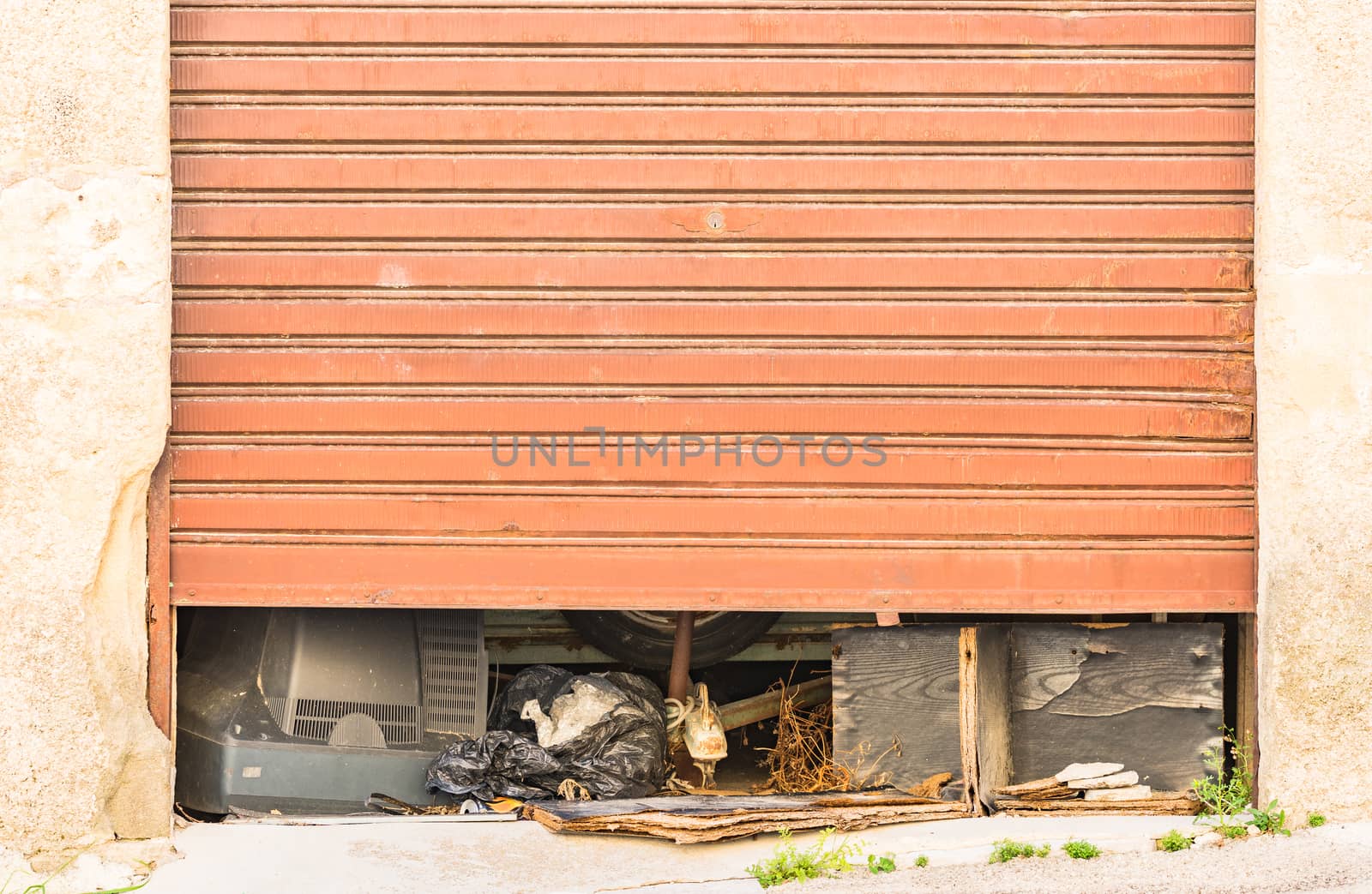 View of half-open old rolling gate garage with garbage