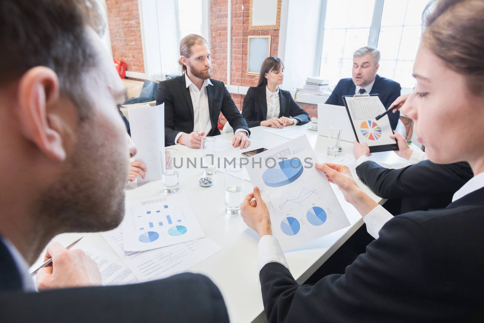 Business, people, statistics and team work concept - creative team with charts on paper, smartphones and tablet pc computers sitting at table in office