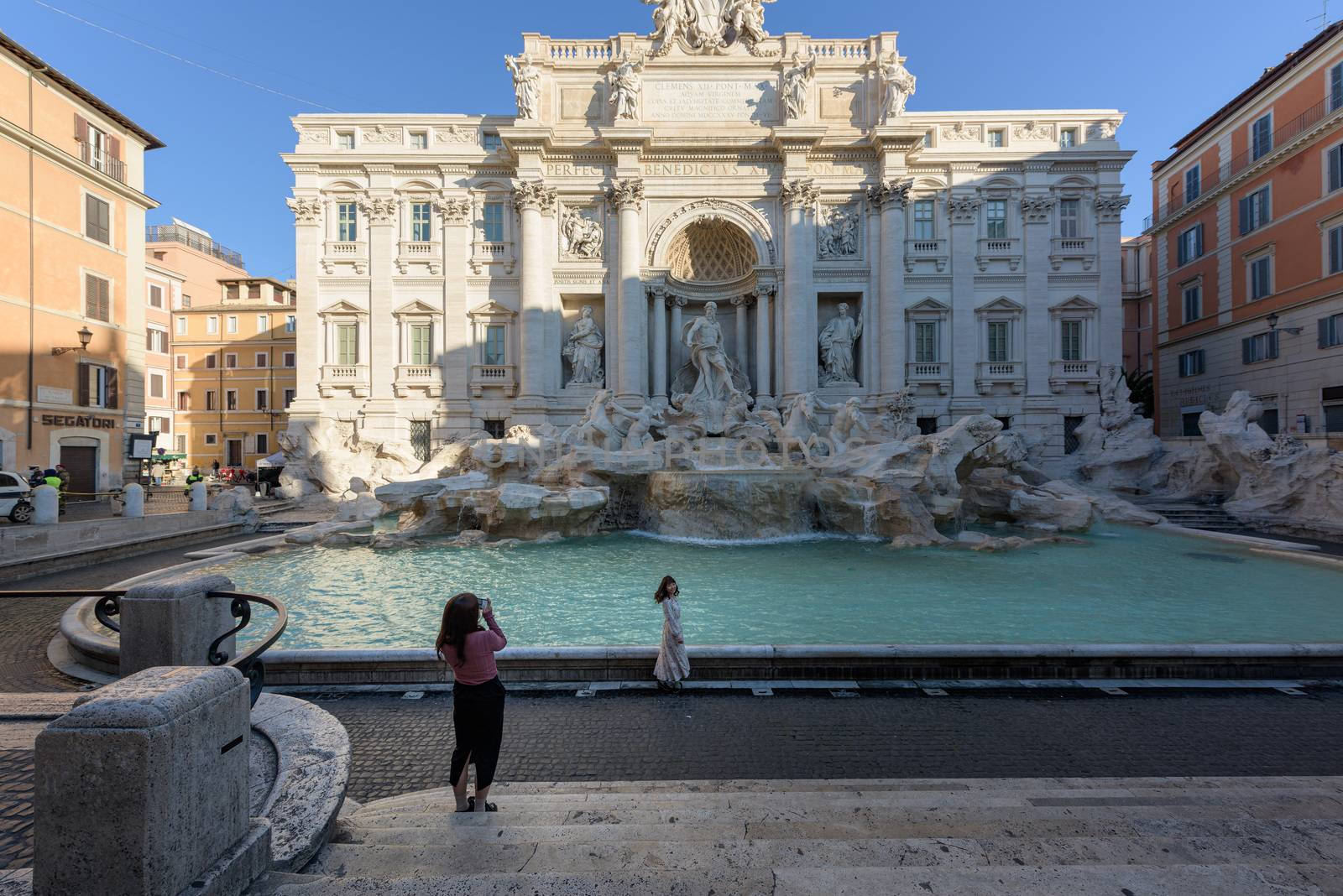Rome, Italy - 10 March 2020: Two lone tourists take pictures in front of the deserted Trevi Fountain, a rare sight today in Rome, Italy. As of today, the Italian government decreed a nationwide quarantine, with travel and gatherings bans, limited opening hours for shops and venues, and emergency health measures following the CoVid-19 epidemic. Tourism has collapsed as a result.