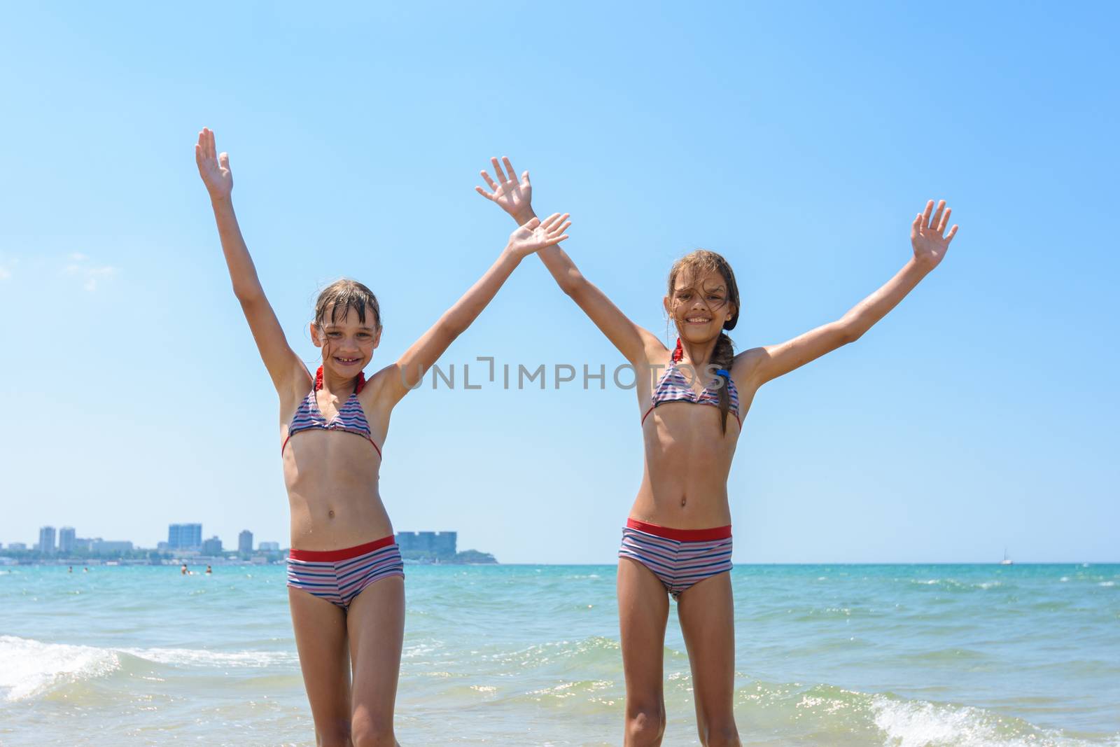Two girls joyfully raised their hands up on the seashore