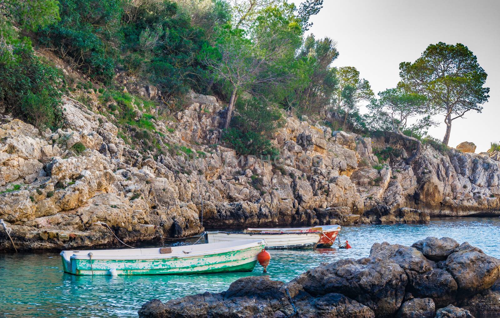 Tranquil scene with two old fishing boats moored in sea water at rocky coast