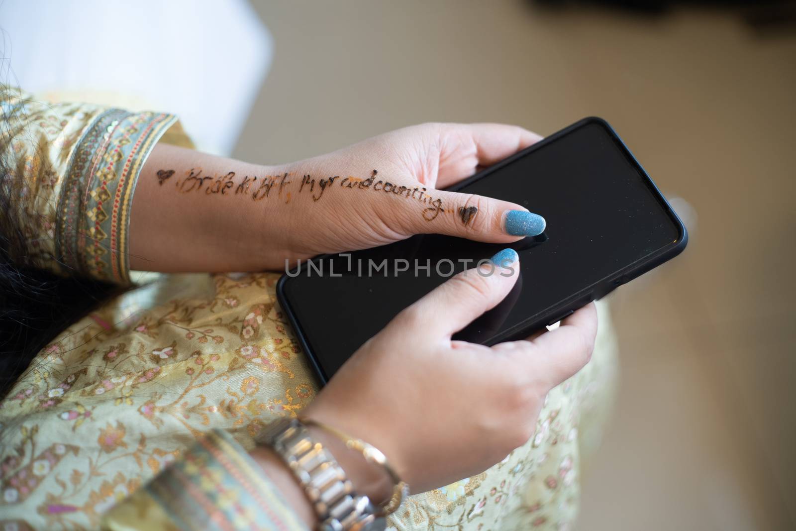 Young indian girl decked in white gold dress preparing for a wedding holding phone with words bride to be BFF written in henna tattoo. Shows the preparation for a indian wedding by the bridesmaids