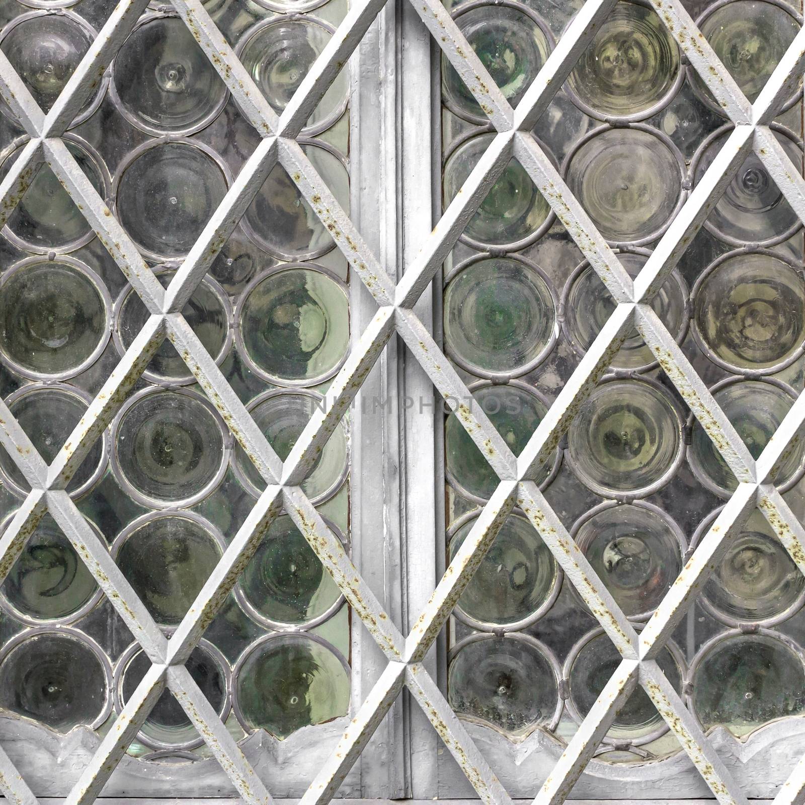 Window with white grate on background of matt glass with pattern of circles. Retro style and faded tones.