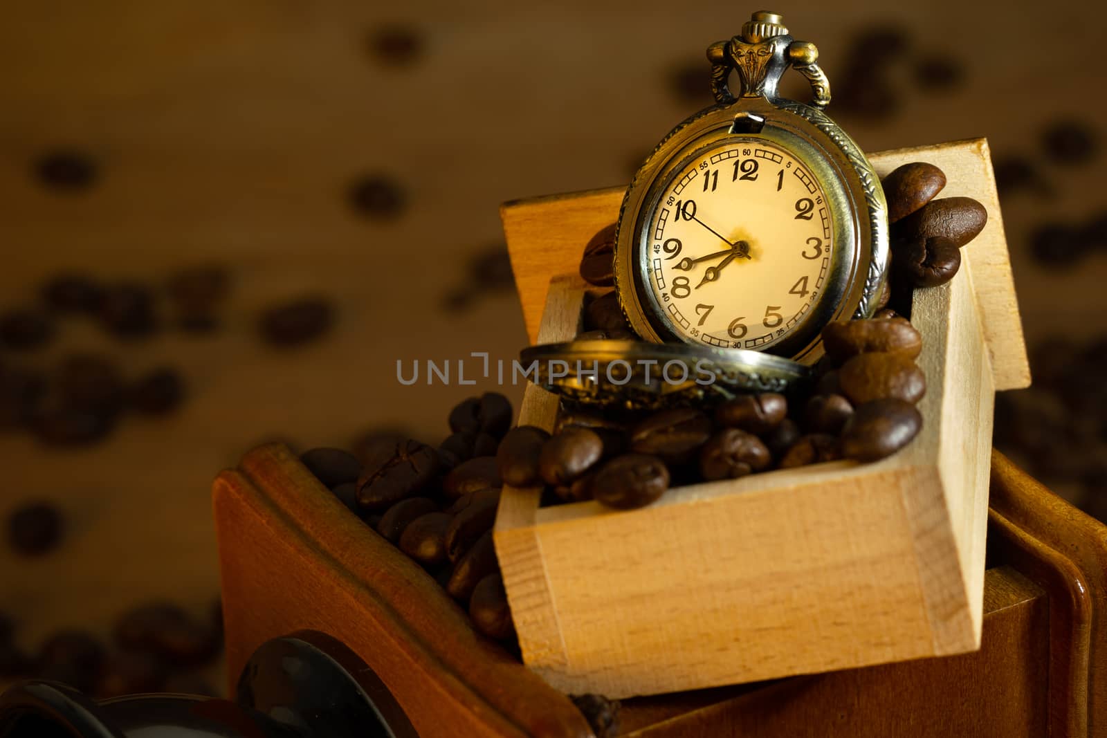 Coffee bean and pocket watch in manual grinder on table. Closeup and copy space. Concept of coffee time in morning.