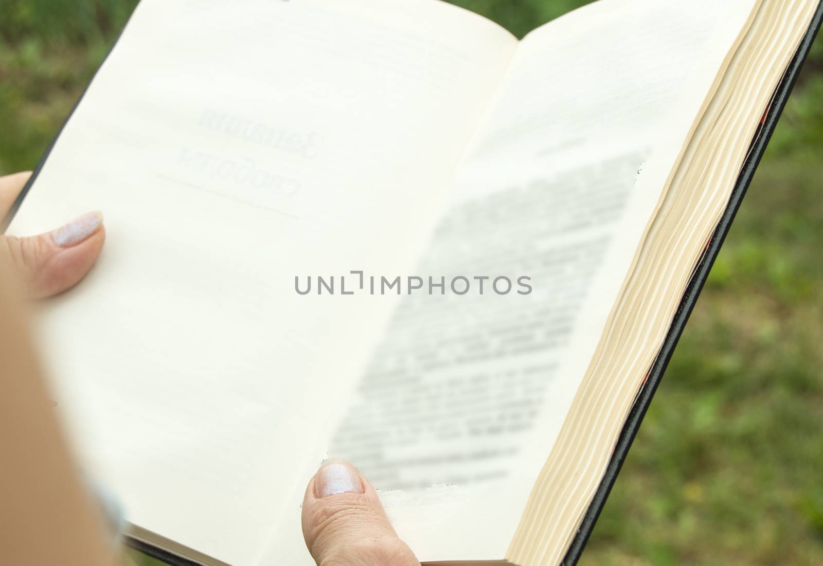 Open book in the hands of a woman, a girl reading a book, view from the back, outdoor, summer.