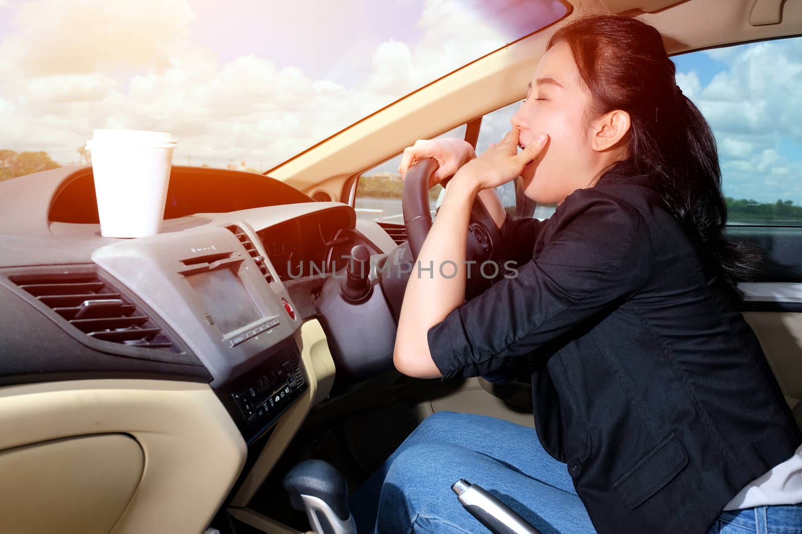 Young woman yawning while driving to work in the morning