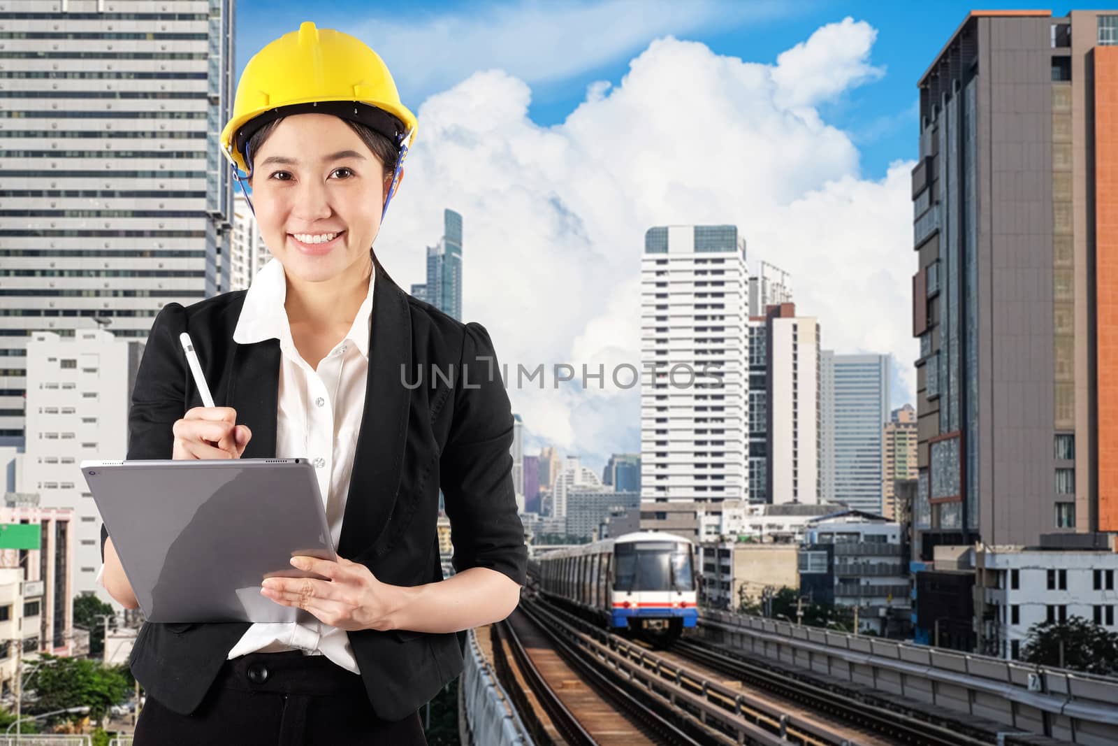 Young woman engineer holding digital tablet wtih smile in city skytrain background