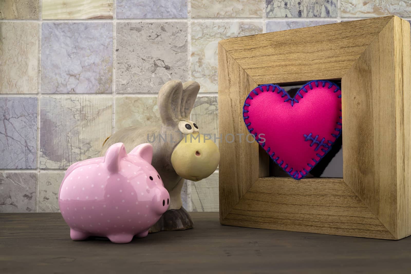 Cute little piggy bank and toy donkey with a handcrafted pink heart in a wooden frame against a tiled background