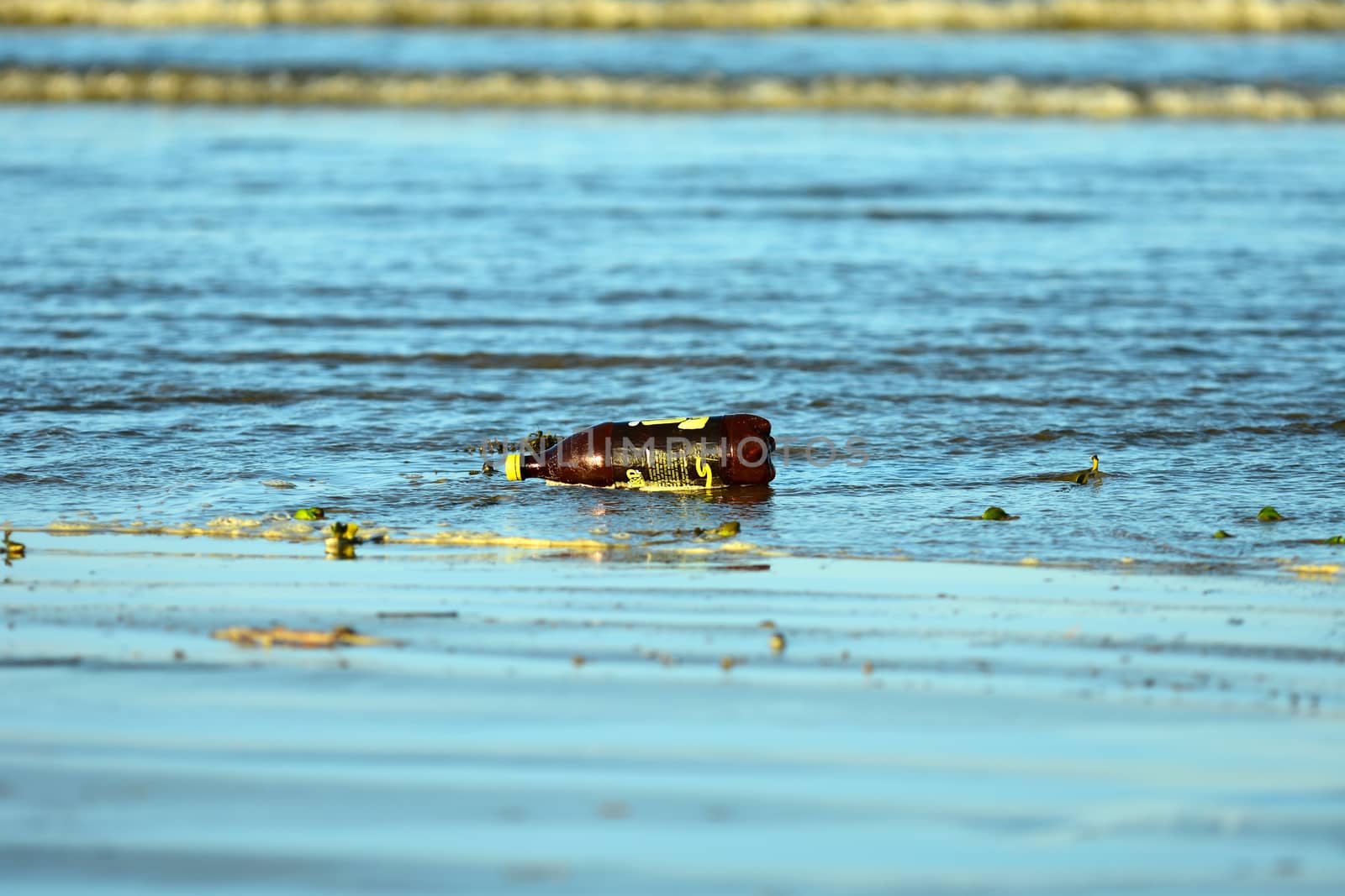 Sea pollution, with a plastic bottle washed ashore on a beach.