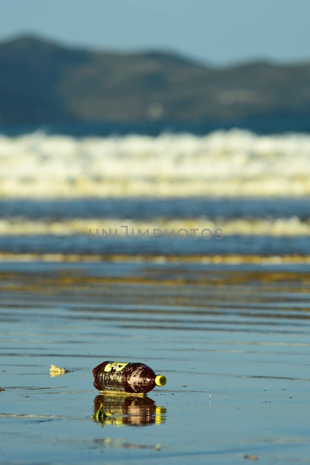 Sea pollution, with a plastic bottle washed ashore on a beach.