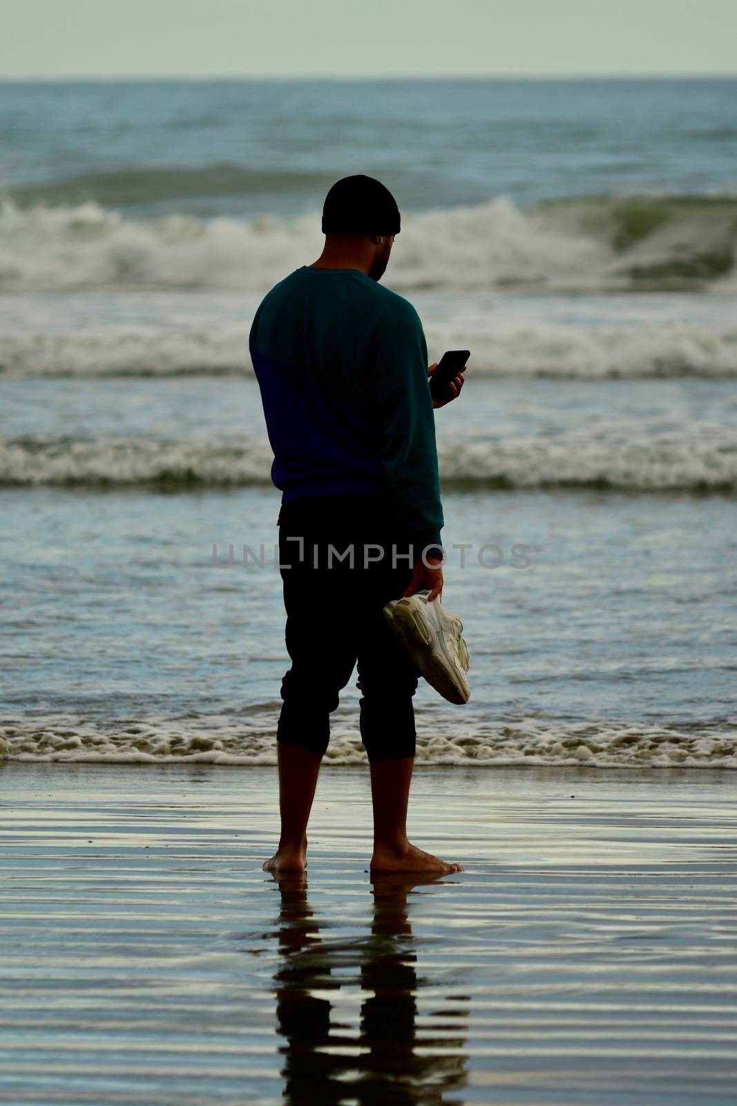 Leisure activities; walking on a beach; a man reading on his phone; taking a photo with a phone camera