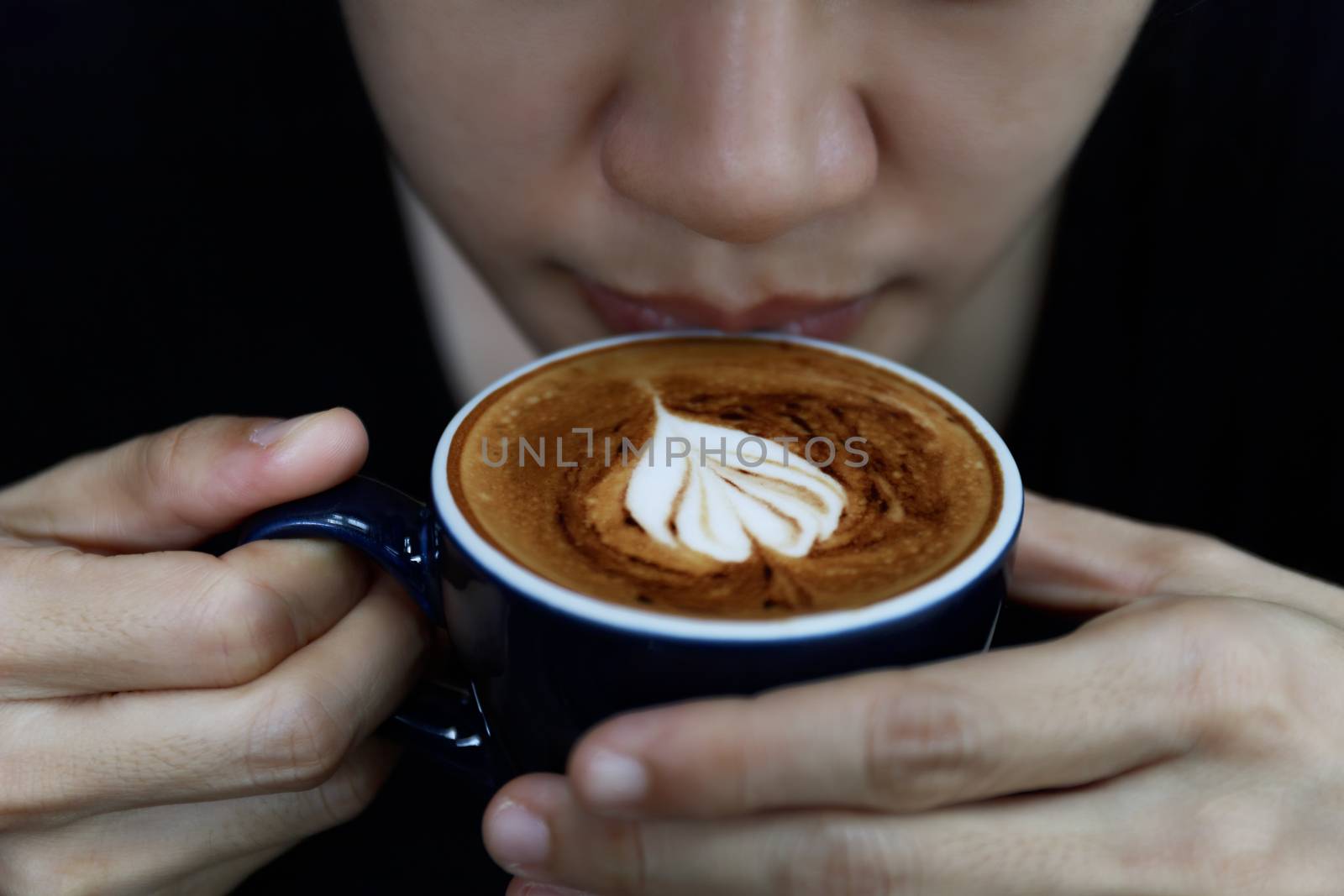 Close up of hot cappuccino coffee in the cafe, Heart shape cream coffee in blue cup. Hands women holding hot coffee in cup Asian woman smelling and drinking hot coffee with feeling good in coffee shop