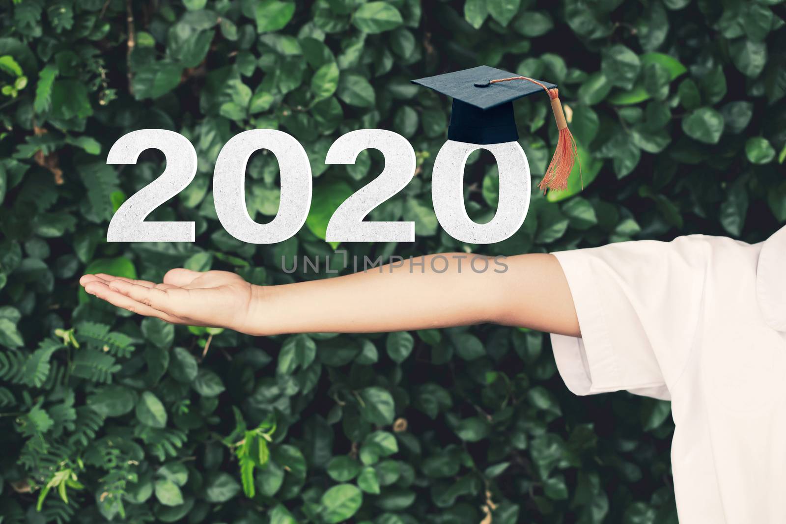 Schoolgirl outstretched arms with Class of 2020 with graduation cap on green nature background