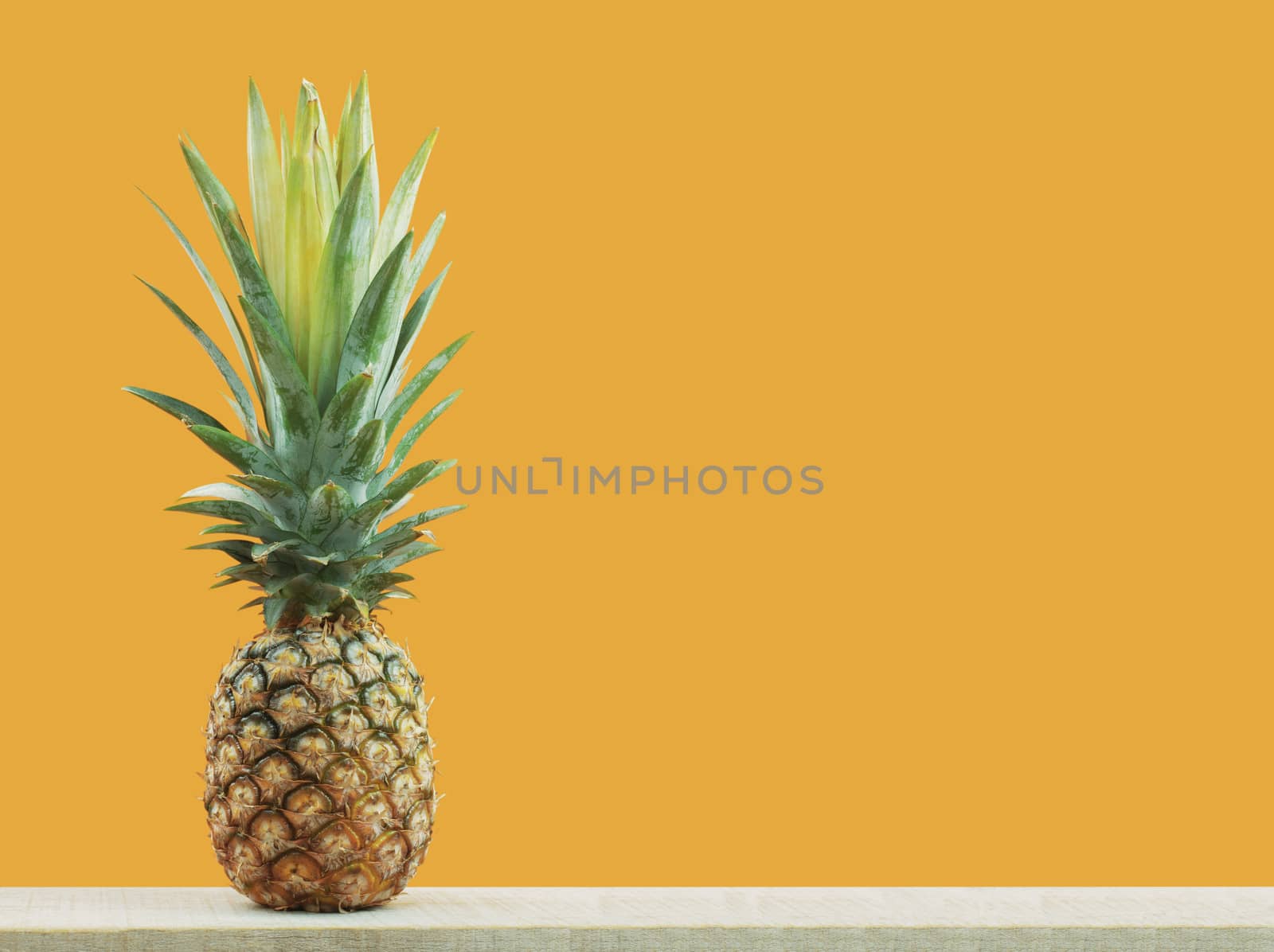 Pineapple on wood with yellow background.