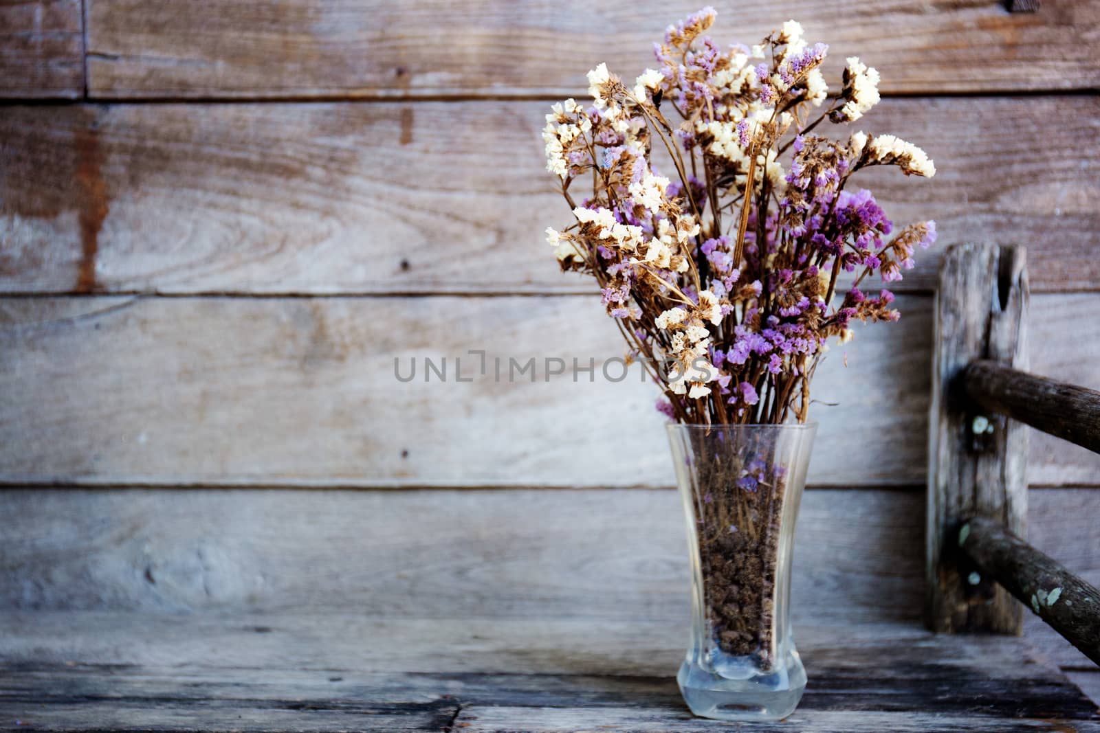 Glass of vase and dry flower on wooden table.