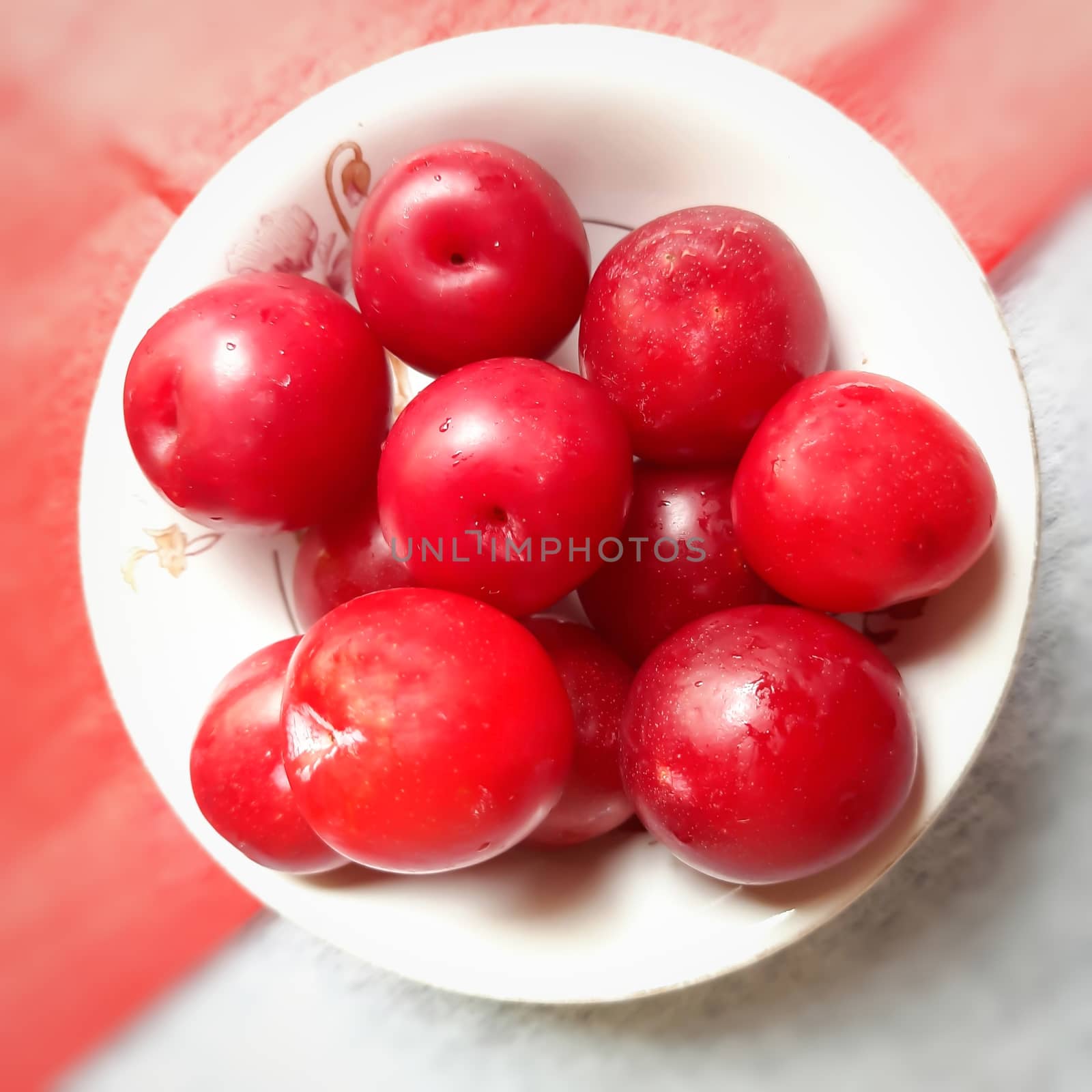 Colorful Red plums kept in bowl placed in red and white backgrounds and reduce the risk of cancer heart disease and diabetes by AnithaVikram