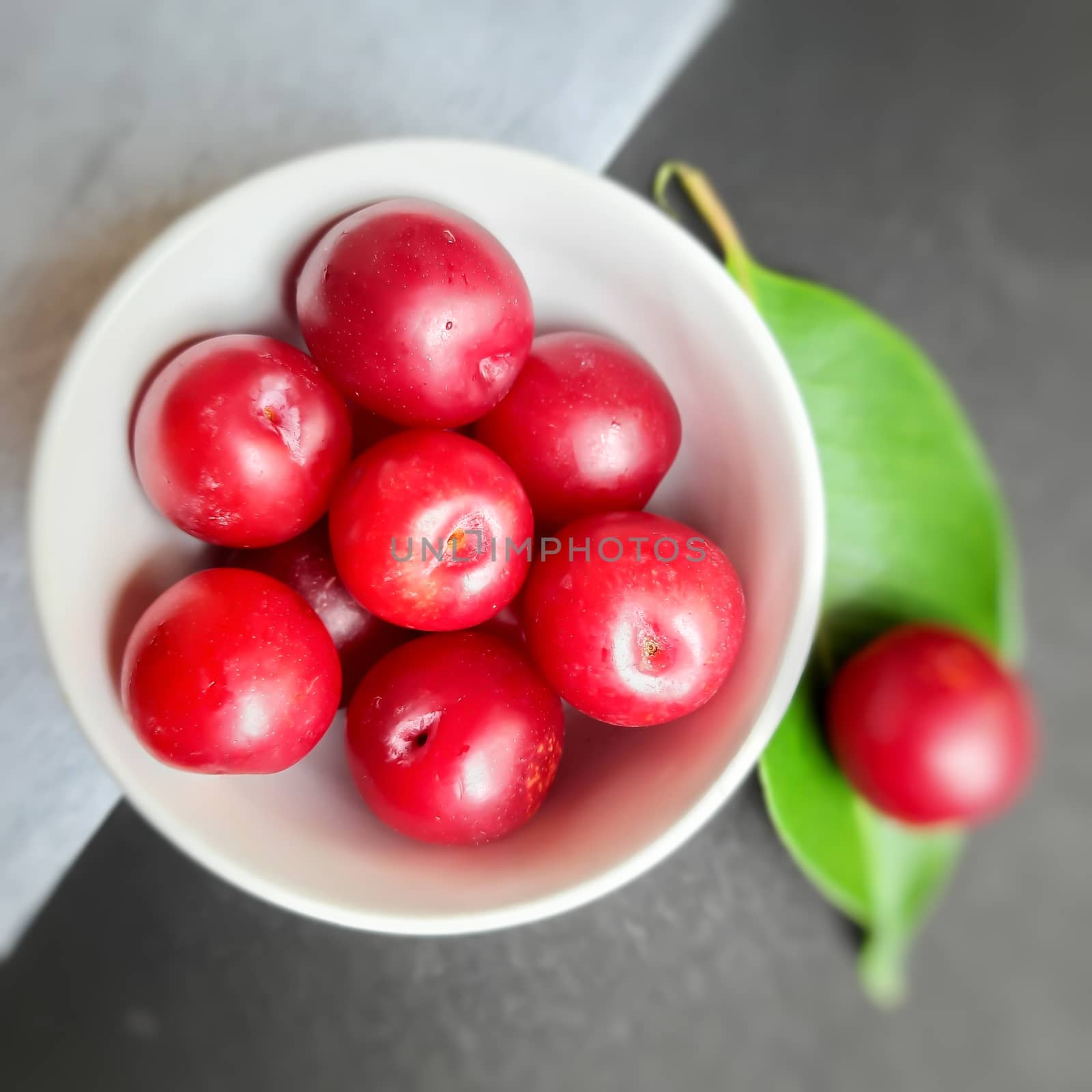 Colorful Red plums kept in bowl with leaves placed in white and black background and reduce the risk of cancer heart disease and diabetes by AnithaVikram