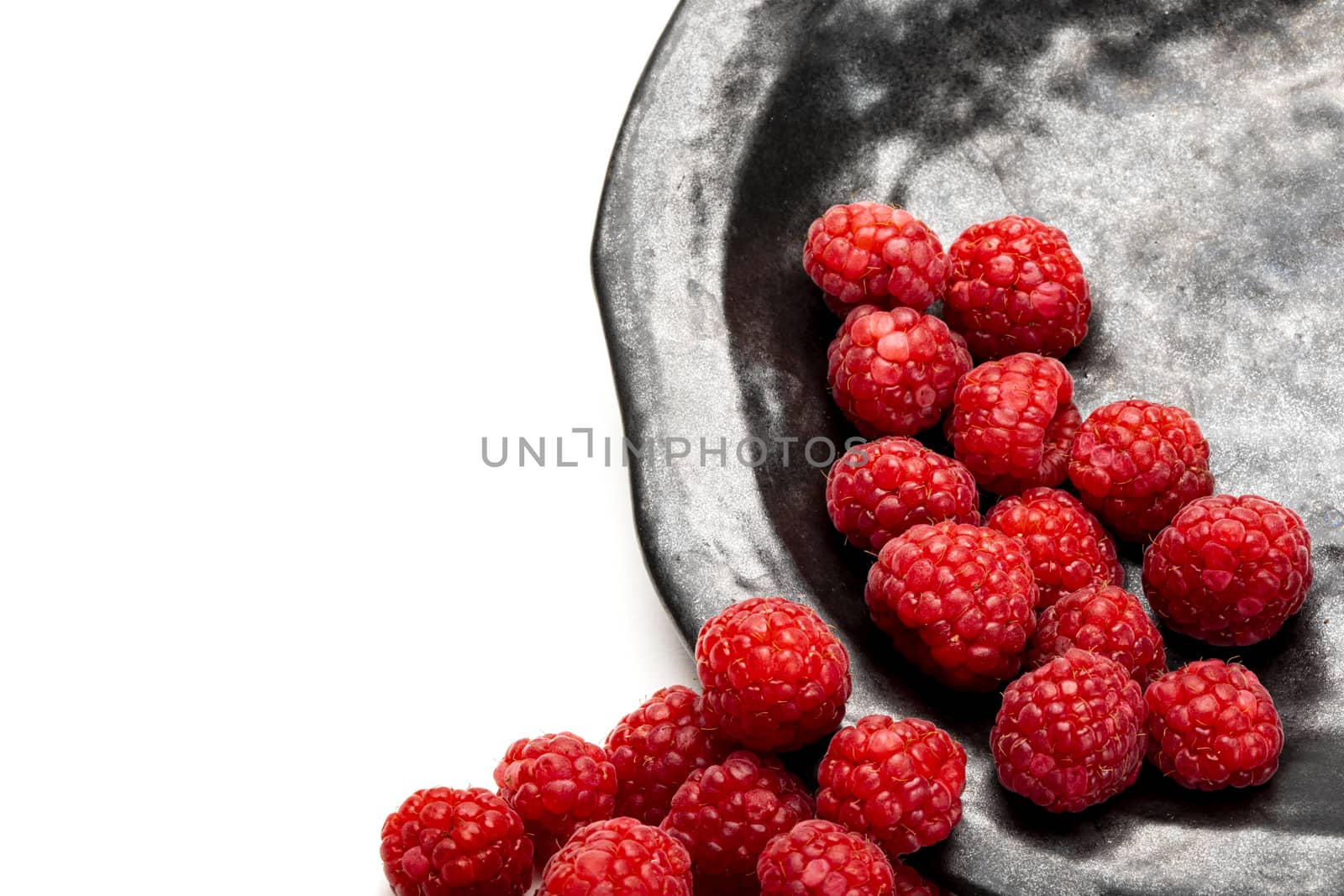 Fresh raspberries on a charcoal black plate. Isolated on white background.