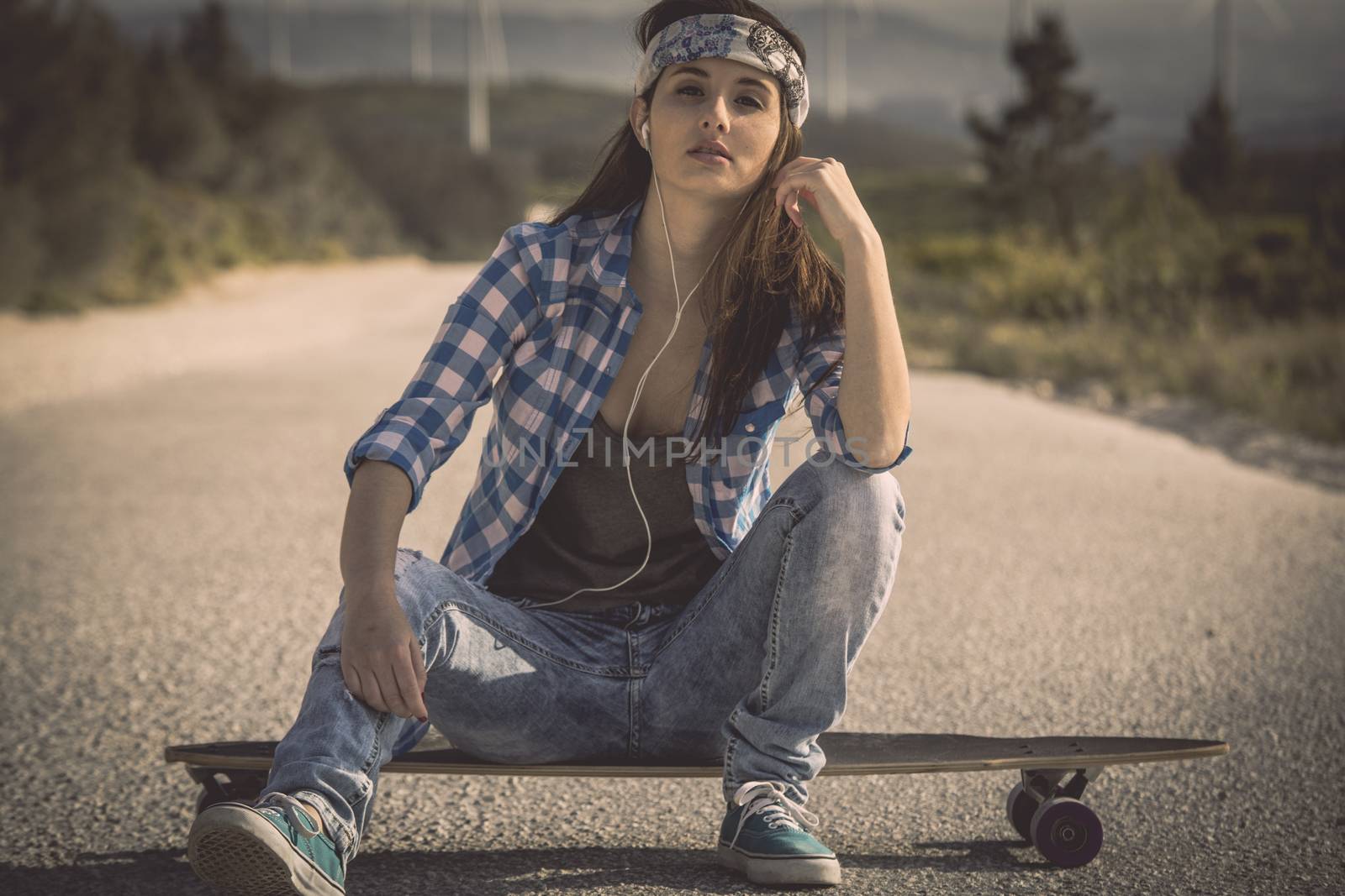 Beautiful young skateboarder girl sitting over her skate