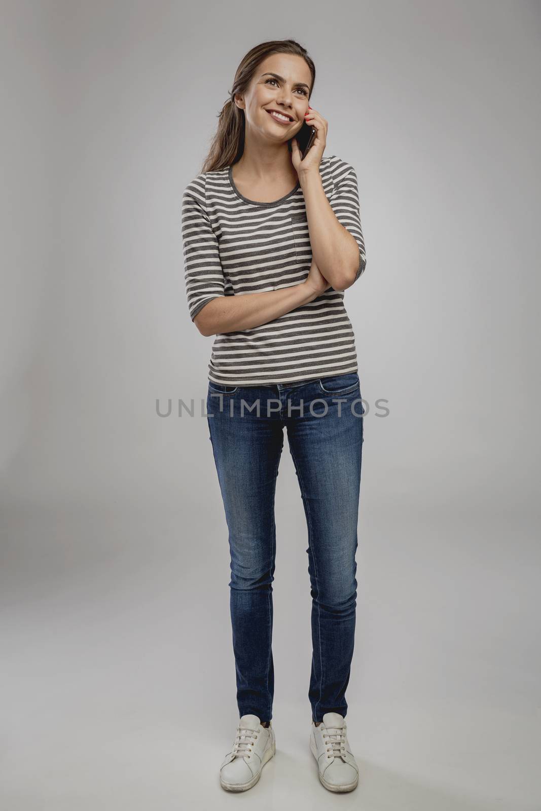 Portrait of beautiful happy young woman over a gray background talking at phone
