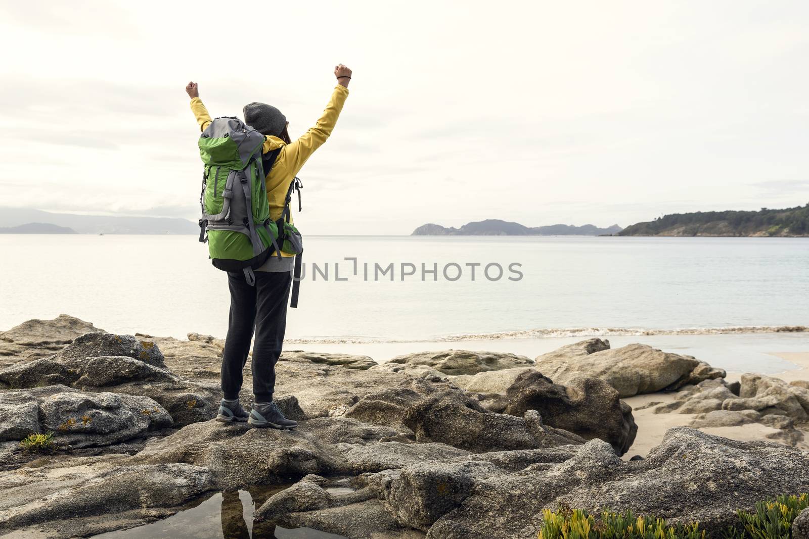 Woman with backpack and arms raised  enjoying the beautiful morning view of the coast