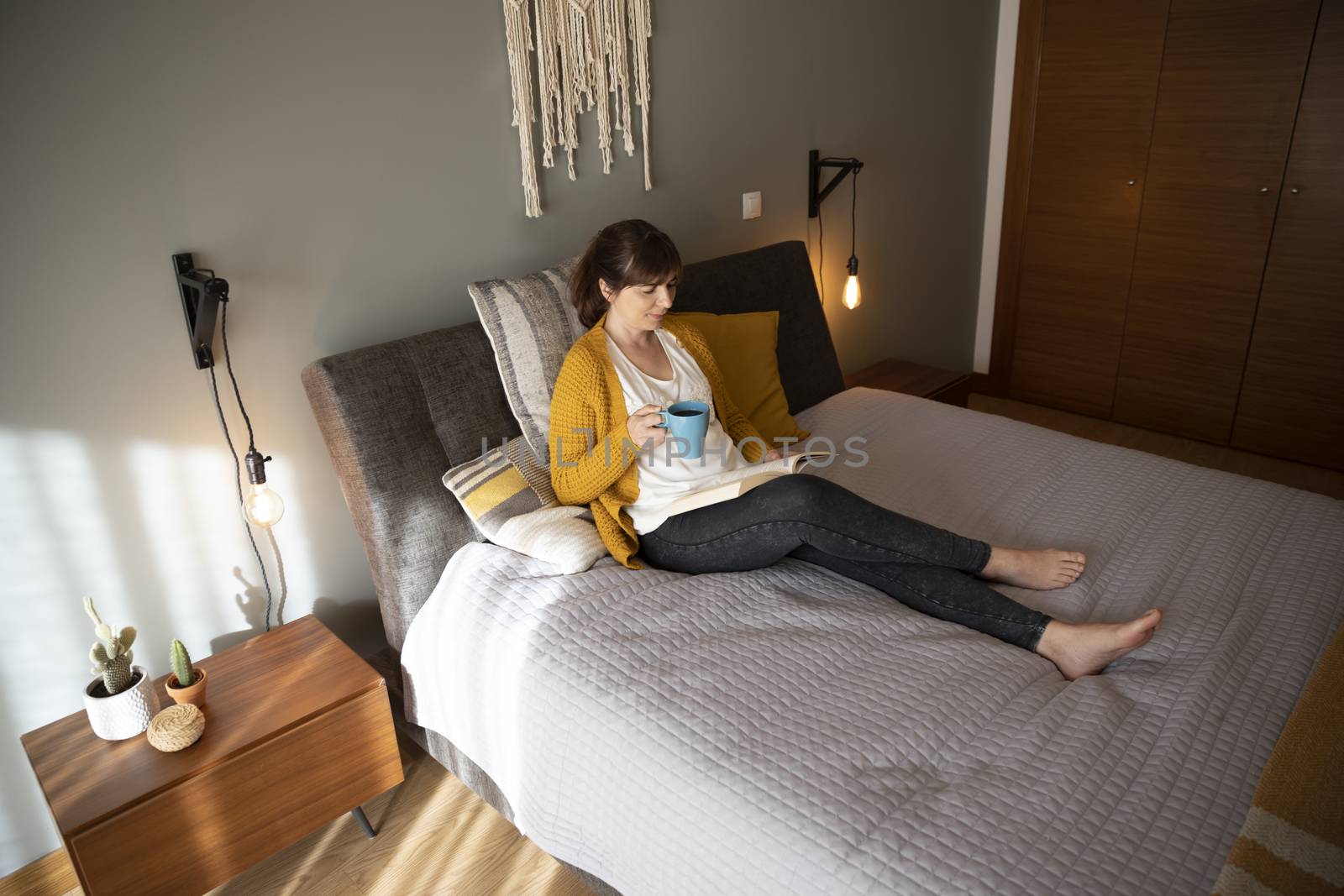 Beautiful woman on bed with a cup of coffee and reading a book