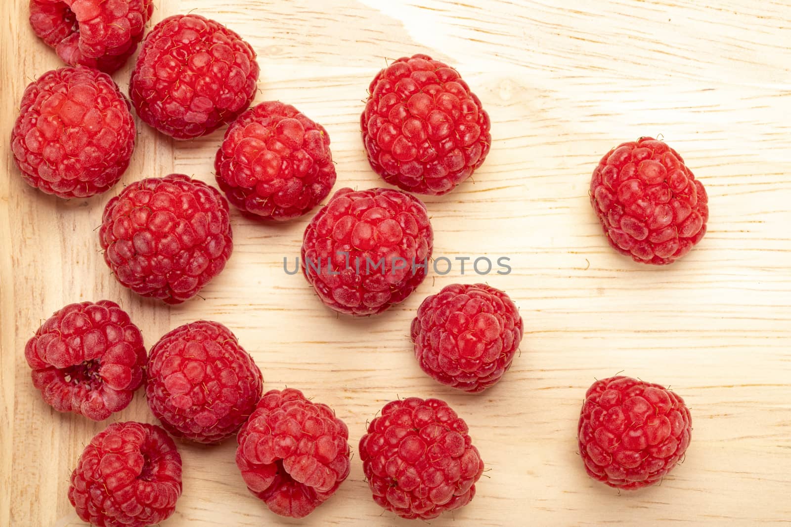 Fresh ripe raspberries on a wooden plate.