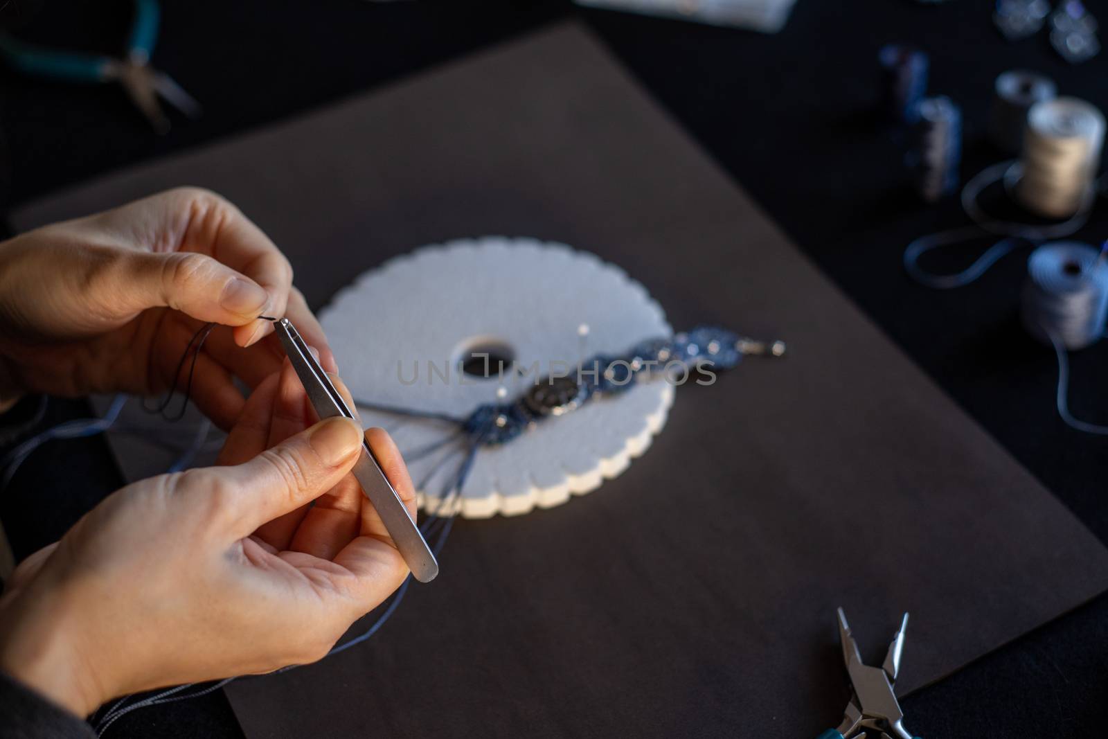 Lifestyle concept, reinvent your life and your job: close-up detail of woman hands making macrame knotted jewel with the fingers threading the bead into the nylon thread on black work table by robbyfontanesi