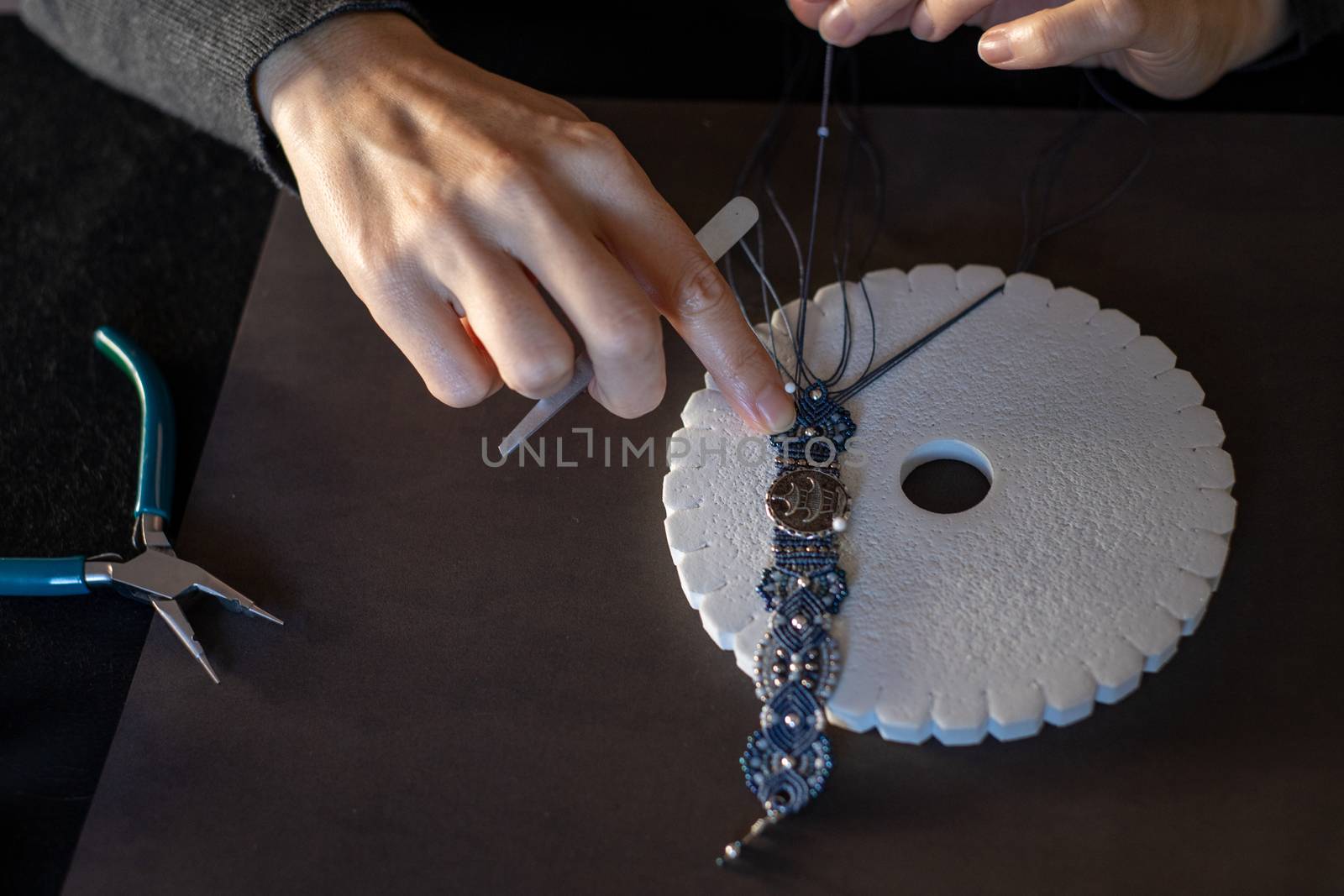 Lifestyle concept, reinvent your life and your job: close-up detail in low angle view of woman hands making macrame knotted bracelet with the fingers knotting the nylon thread on the kumihimo by robbyfontanesi