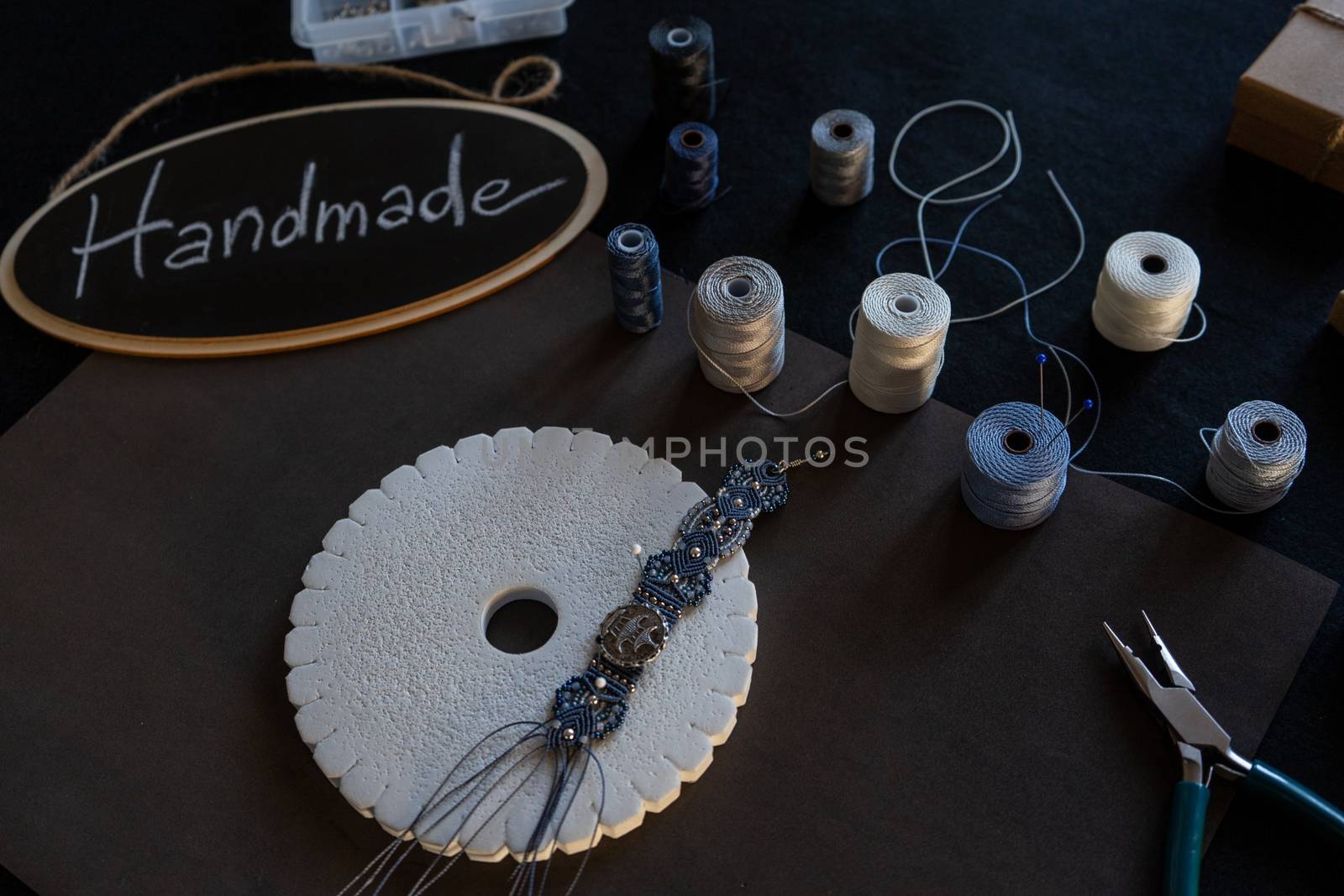 Lifestyle concept, reinvent your life and your job: angle top view of macrame jewels with colored spools of thread, a bracelet, beads, tools and a little blackboard with text handmade chalked