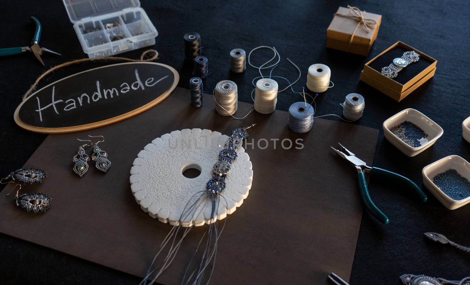 Lifestyle concept, reinvent your life and your job: angle top view of macrame jewels with colored spools of thread, a bracelet, beads, tools and a little blackboard with text handmade chalked