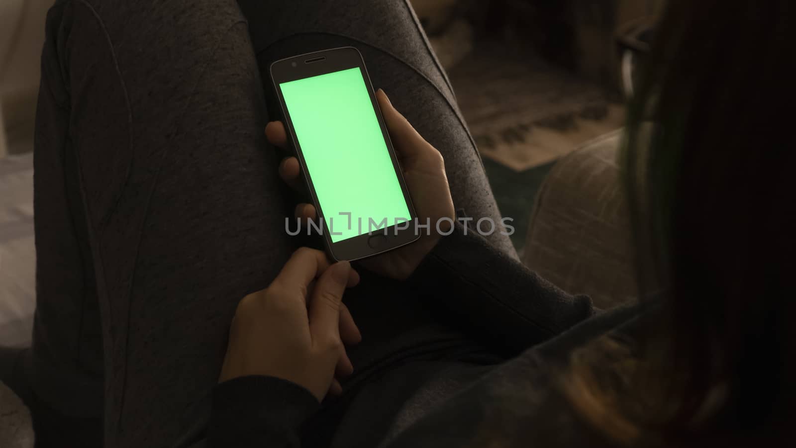 Couple relationships and dating in modern times concept: closeup of woman sitting on her sofa using her smartphone with blank green screen in low light