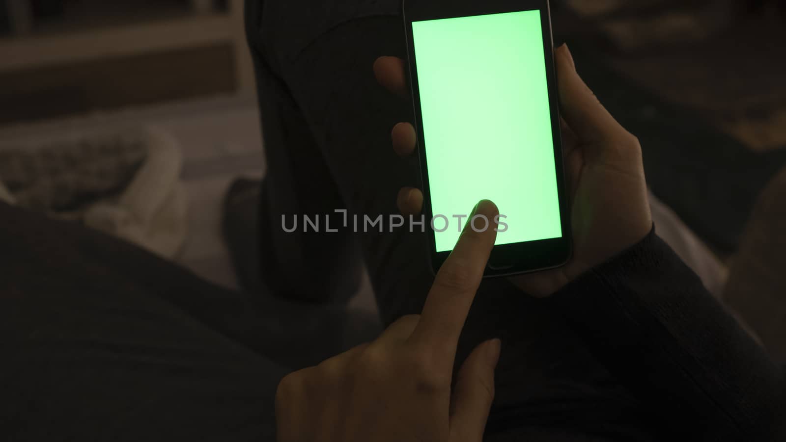 Couple relationships and dating in modern times concept: closeup of woman sitting on her sofa using her smartphone with blank green screen in low light