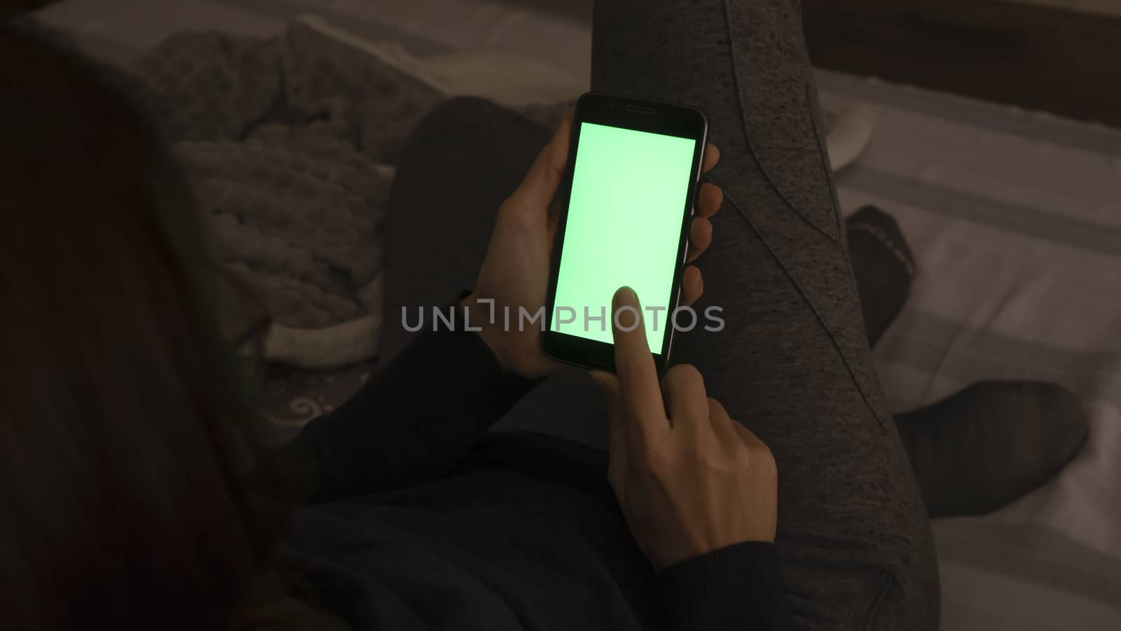 Couple relationships and dating in modern times concept: closeup of woman sitting on her sofa using her smartphone with blank green screen in low light by robbyfontanesi