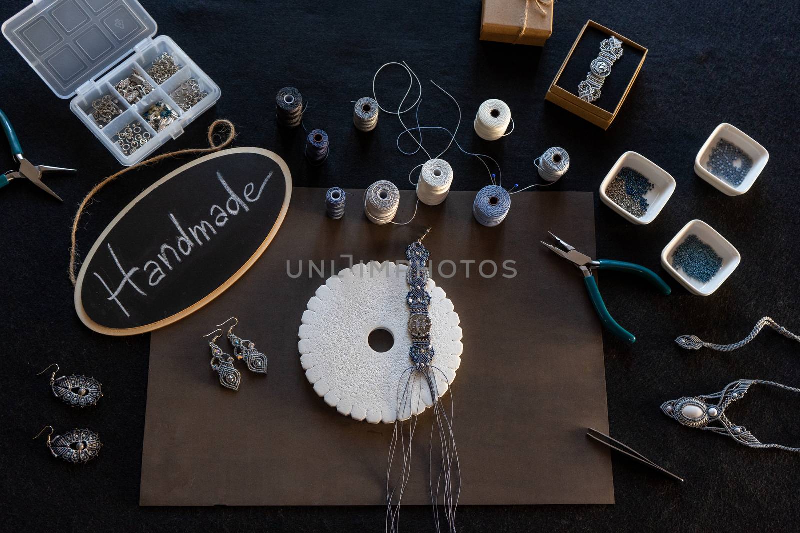 Lifestyle concept, reinvent your life and your job: flat lay top view of macrame jewels with colored spools of thread, a bracelet, beads, tools and a little blackboard with text handmade chalked
