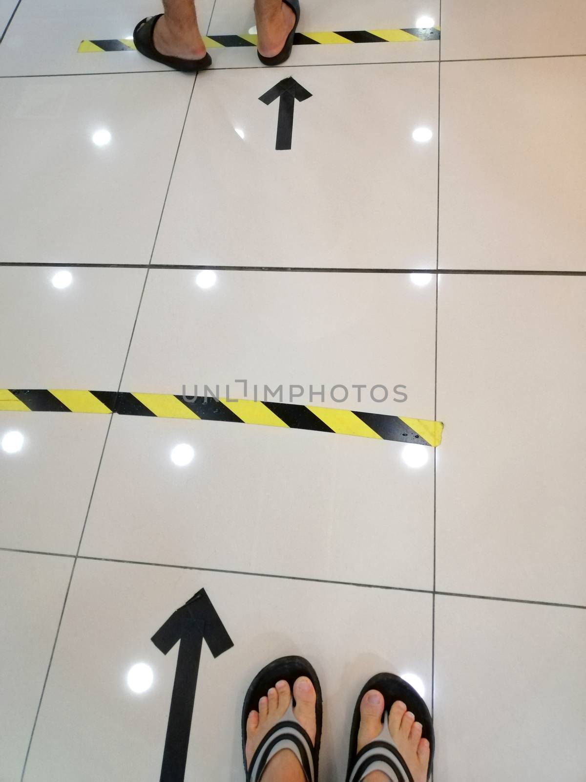 People stand in yellow black footprint  line on the floor of the store to maintain social distance. Concept of the coronavirus pandemic and prevention measures.