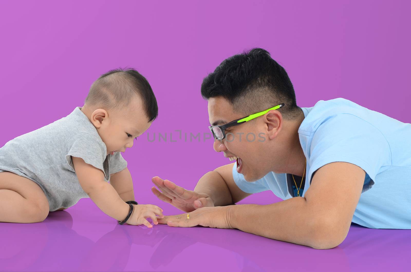 Happy father's day! joyful young dad  playing with  his cute son and lying on floor at home. Isolated on purple background.