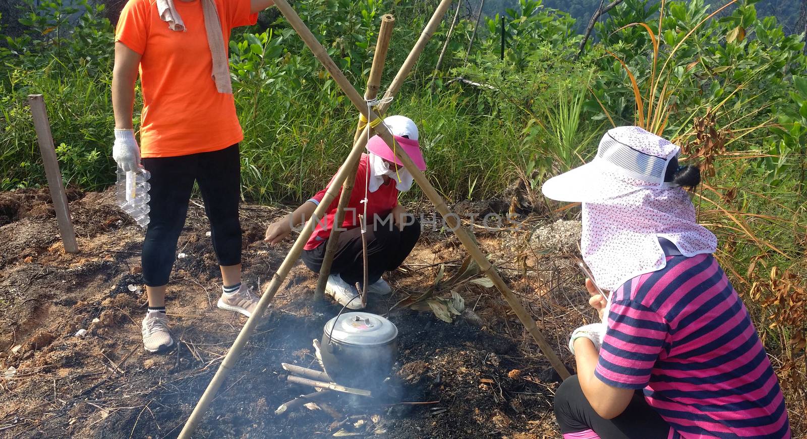 Group of asian hiking girl cooking in a black pot on around a bonfire at outdoor forest.