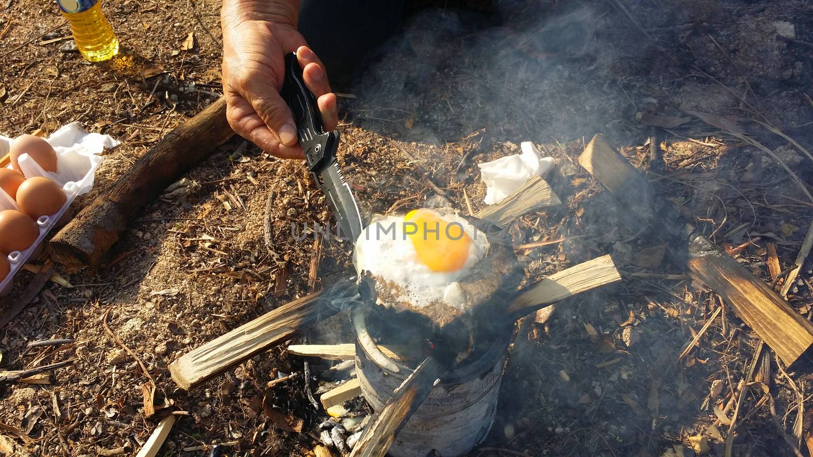 person cooking fried eggs in nature camping outdoor, cooker prepare breakfast scrambled picnic on metal stove.