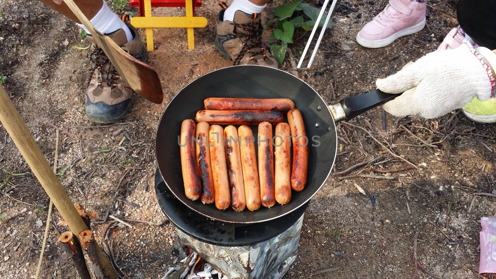 fry sausages on a fire in a pan at forest during summer time.