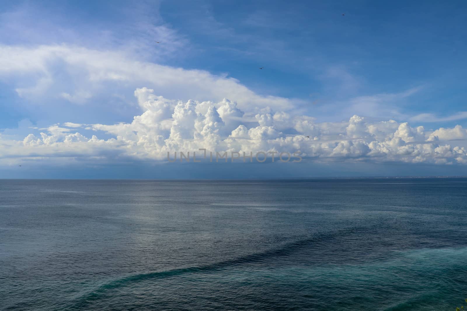Calm sea and blue sky from the side of a boat with bow wave wake and cumulonimbus clouds on the horizon