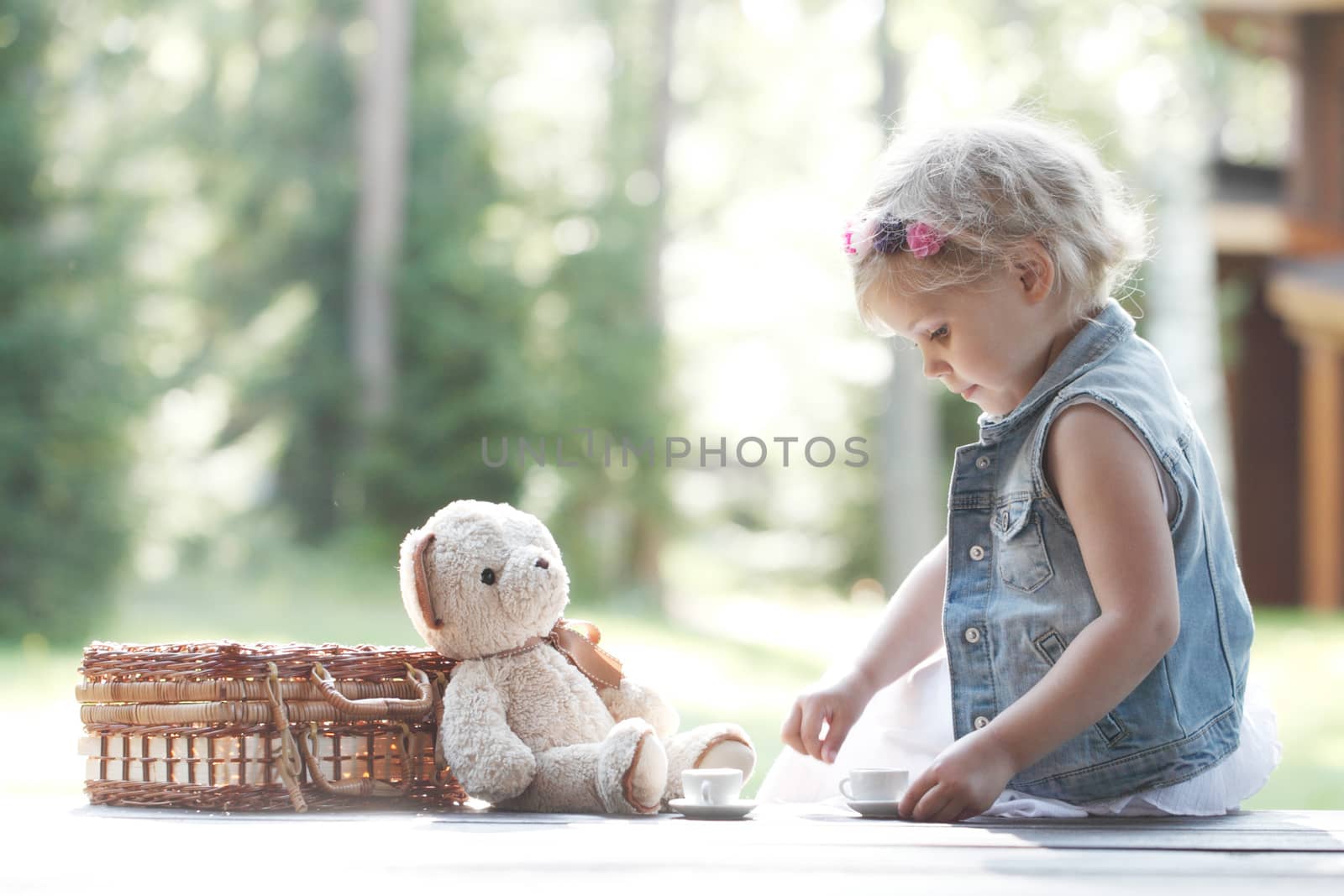 Pretty girl playing with teddy bear outdoors drinking tea