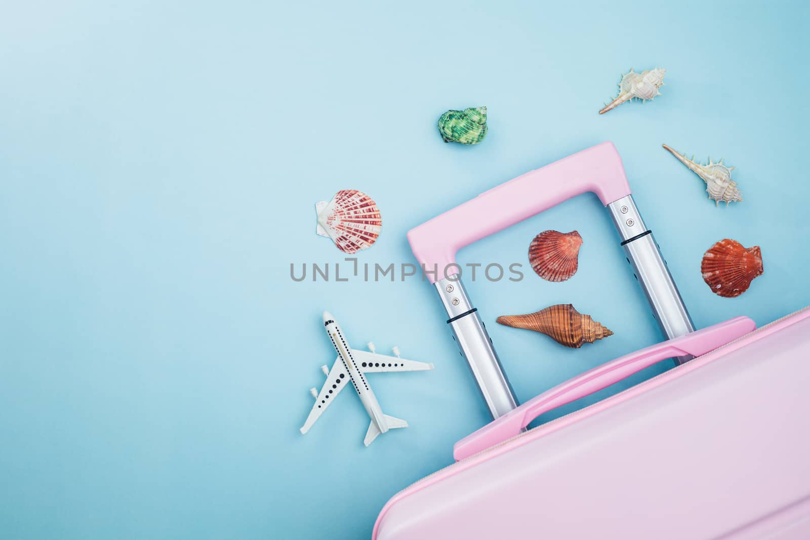 Pink luggage with white airplane model and sea shells on blue background for travelling and summer beach concept