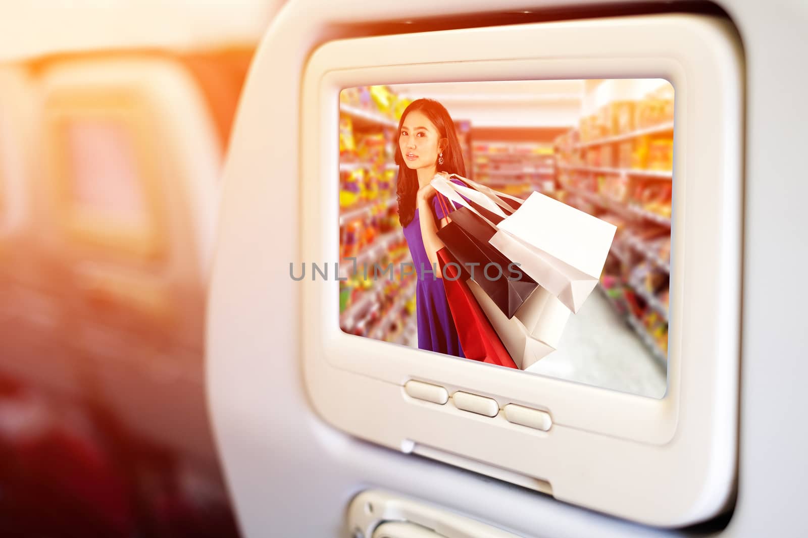 Aircraft monitor in front of passenger seat showing Happy women in blue dress with a shopping bag in shopping mall