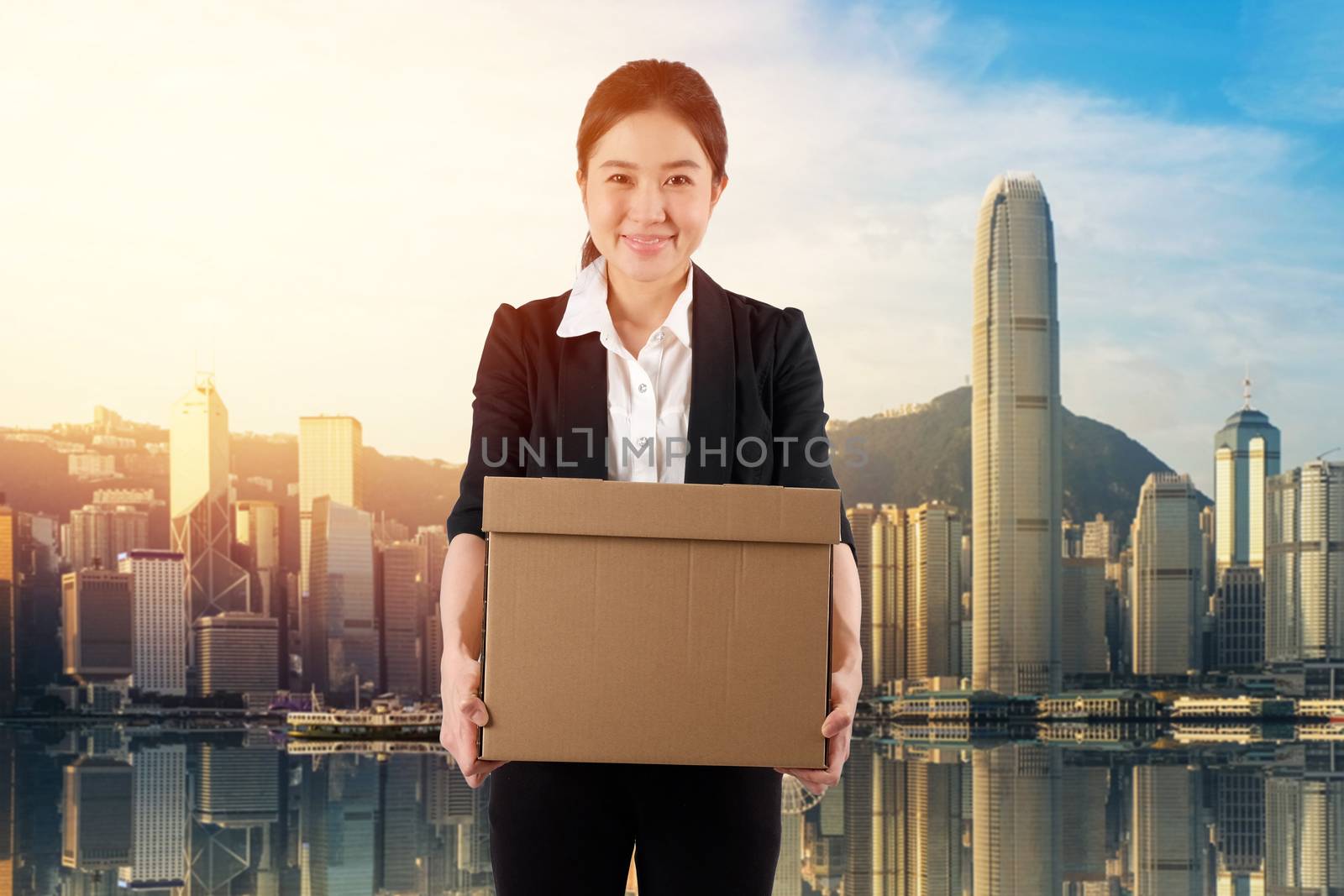 A young woman carrying a box wtih smile in cityscape background
 by Surasak