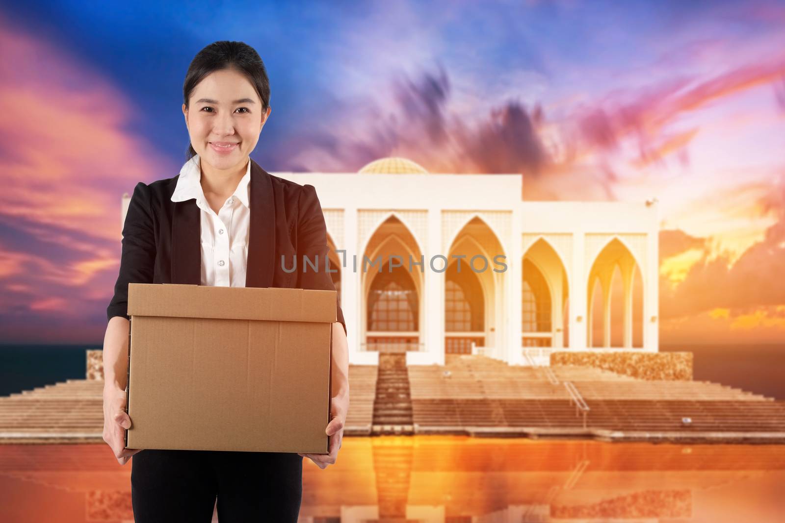 A young woman carrying a box wtih smiling on sunset in mosque background

