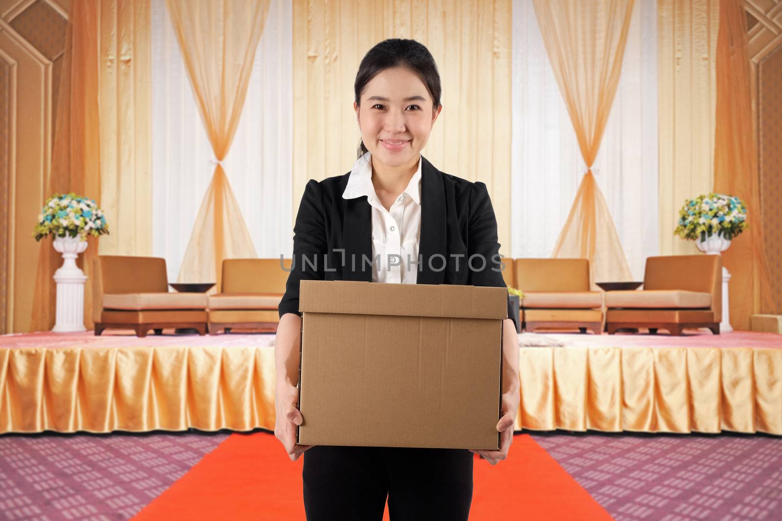 A young woman carrying a box wtih smile in a conference hall