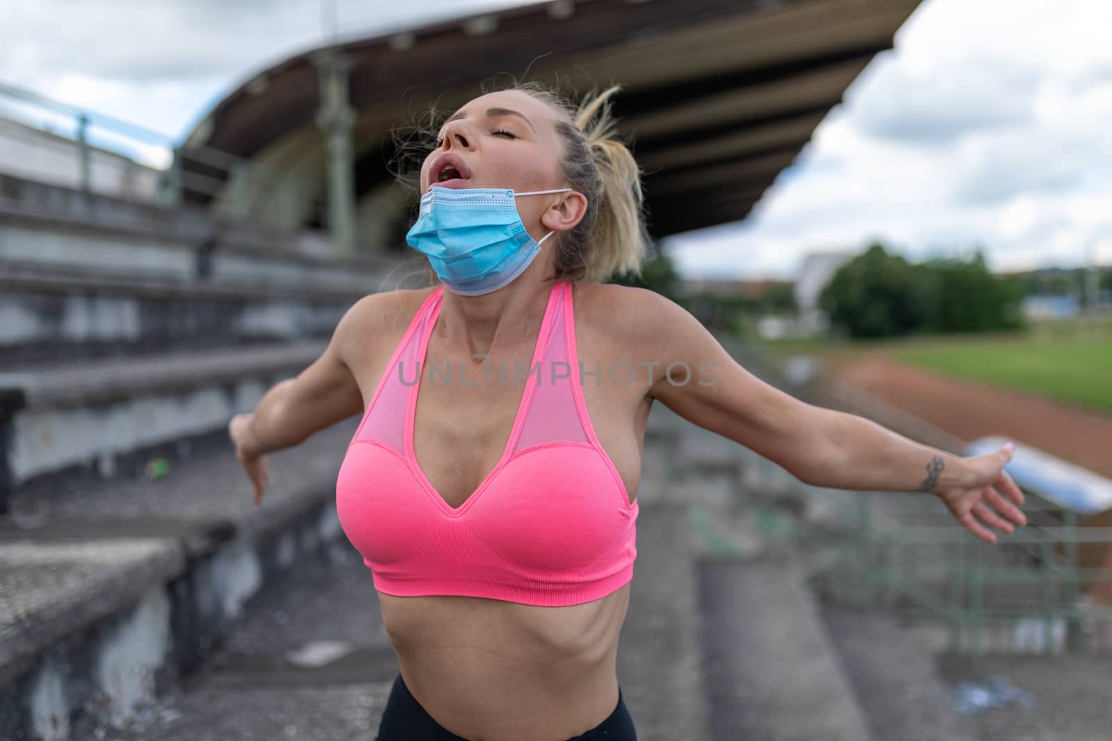 Woman takes off facemask after training or running on sports field. Female breathes deeply